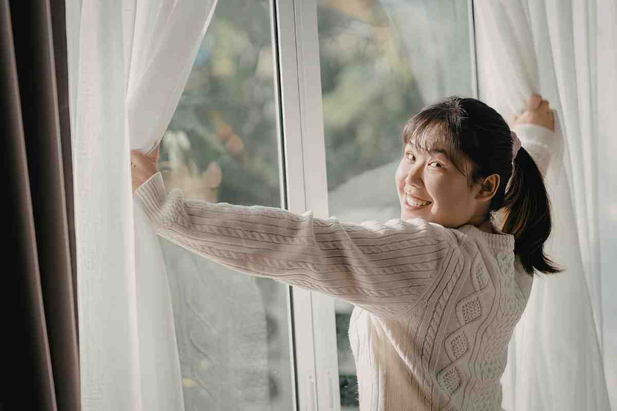 ragazza sposta le tende davanti alla finestra