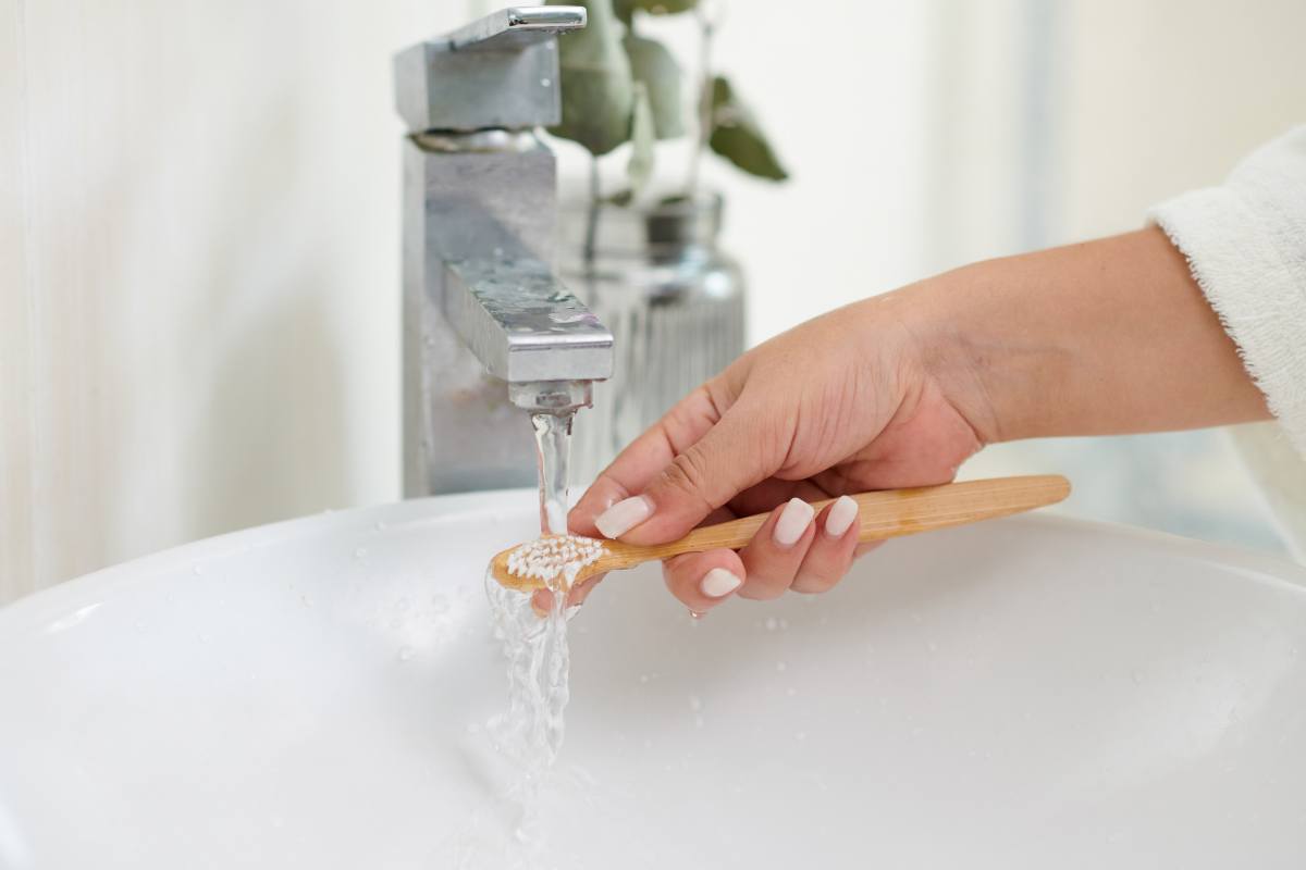 una mano sciacqua lo spazzolino sotto acqua corrente
